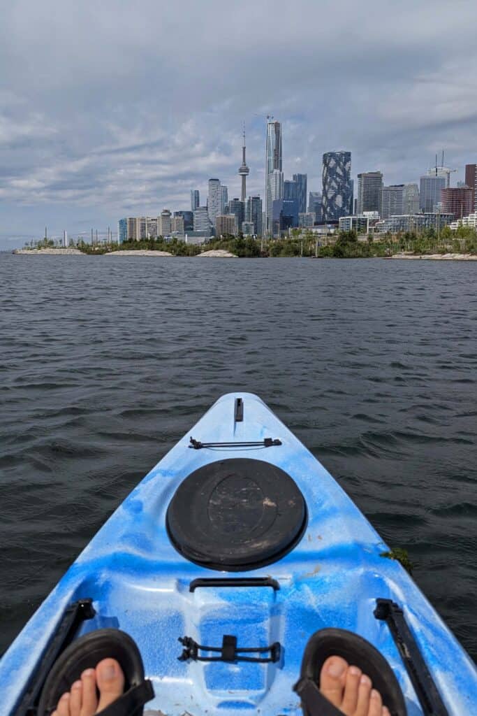 Blue kayak on Lake Ontario with the Toronto skyline, including the CN Tower, visible in the background during a paddling trip.