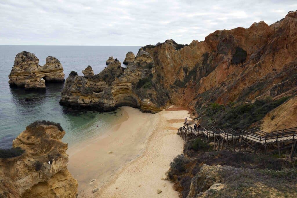 wooden stairs leading down to Praia do Camilo, a sandy beach surrounded by rocky cliffs