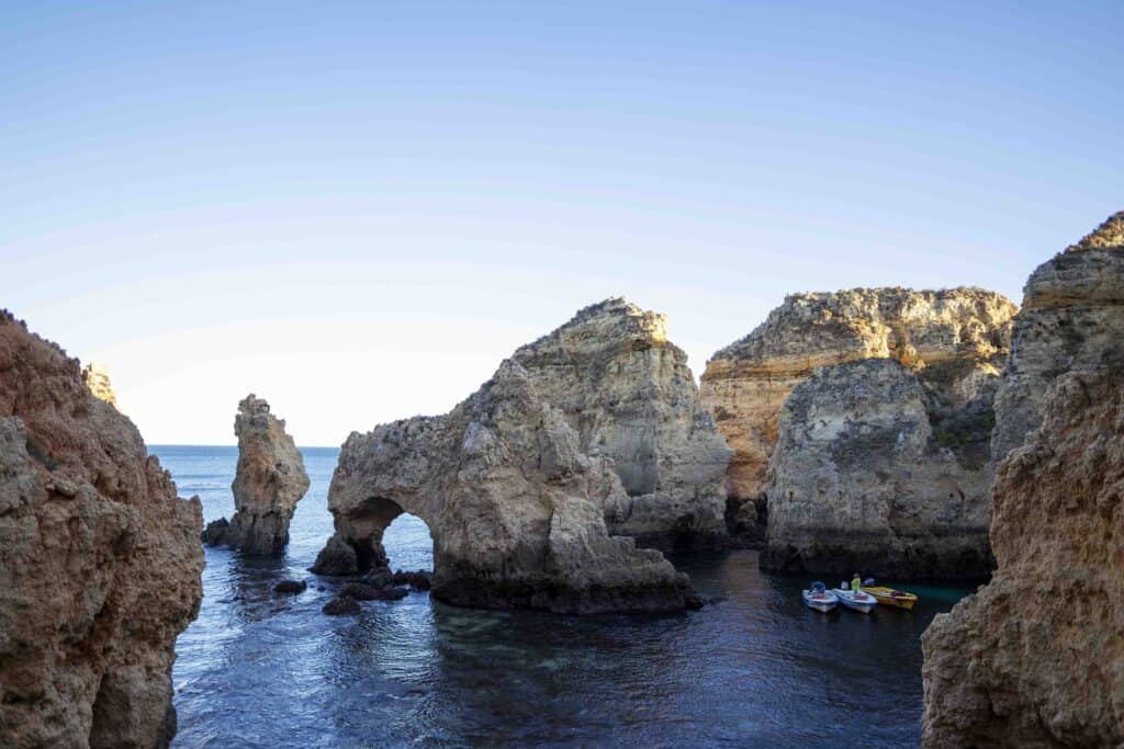 rocks jutting out of. the ocean with small boats amongst them, on the Algarve coast in fall
