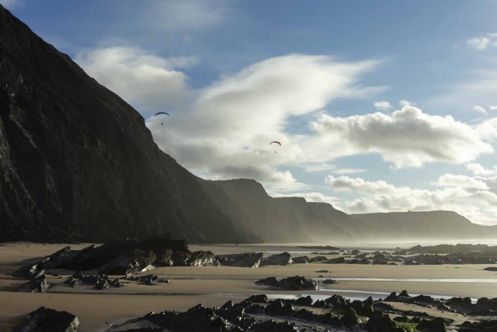 Praia da Cordoama at low tide, with yellow sand, rocks, and cliffs in the distance