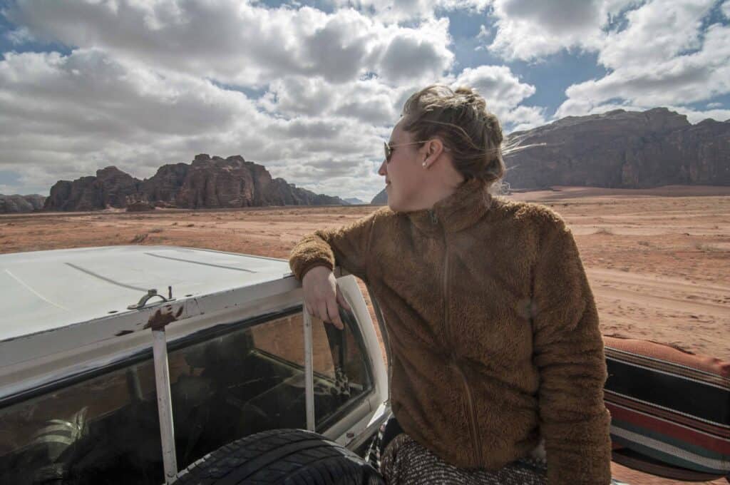 A woman sitting on a truck that's driving through the desert, as an example of a deep travel experience.