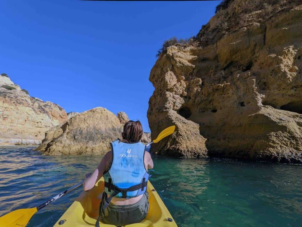 A woman sitting in a sea kayak, paddling the Algarve coast