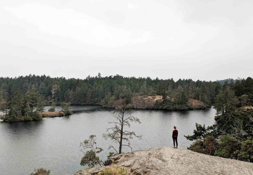 A woman standing on a rock overlooking a lake in Victoria, British Columbia.