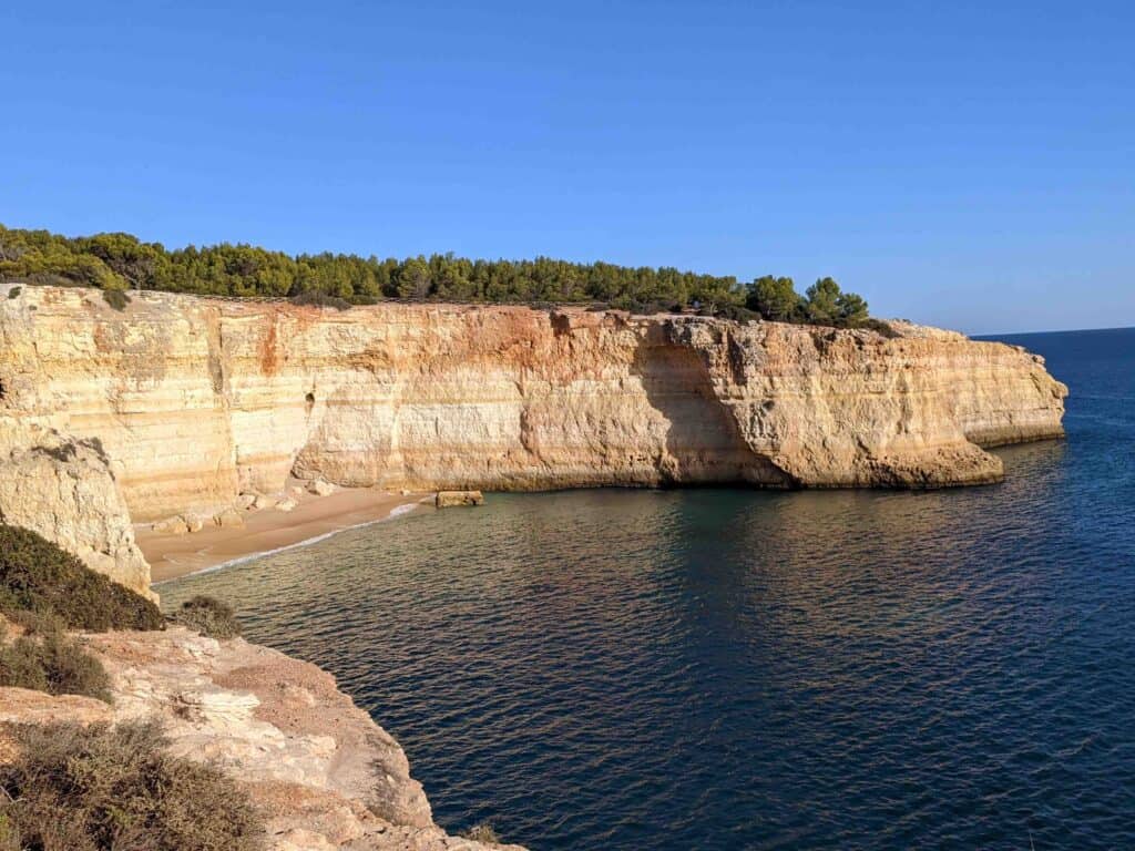 shows a rocky coast, small beach, and blue ocean, part of the Seven Hanging Valleys trail in the Algarve