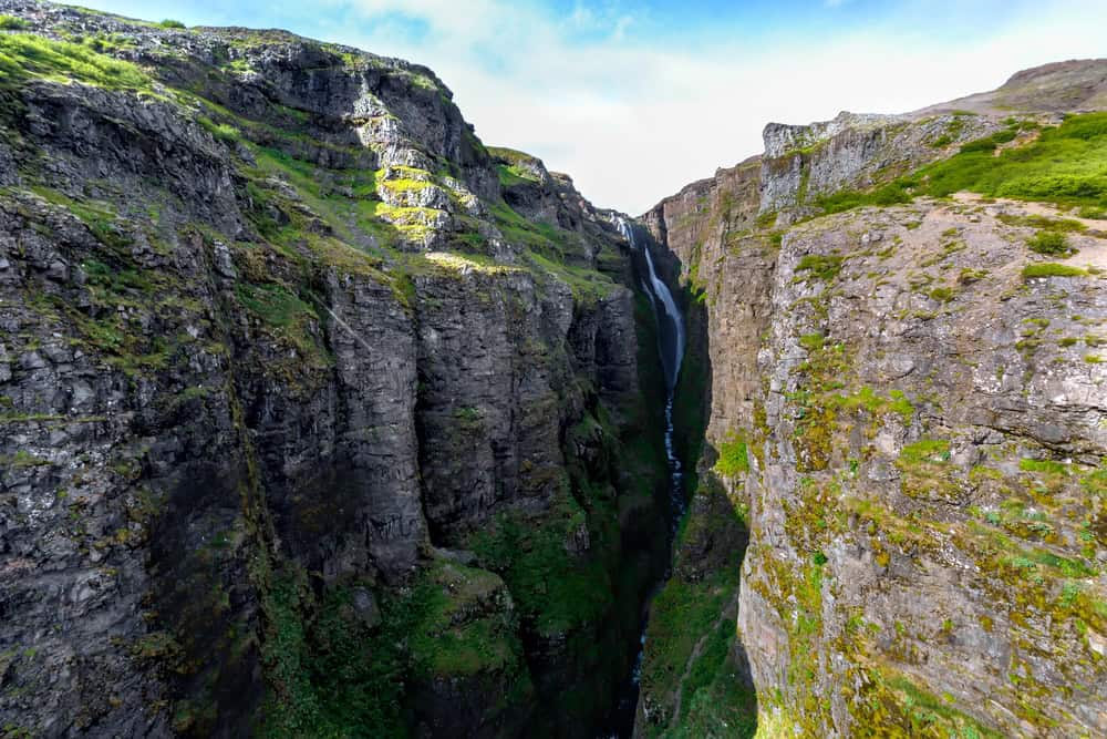 Glymur waterfall plunging into a deep, narrow canyon in western Iceland, surrounded by steep rocky cliffs covered in patches of green moss and vegetation.