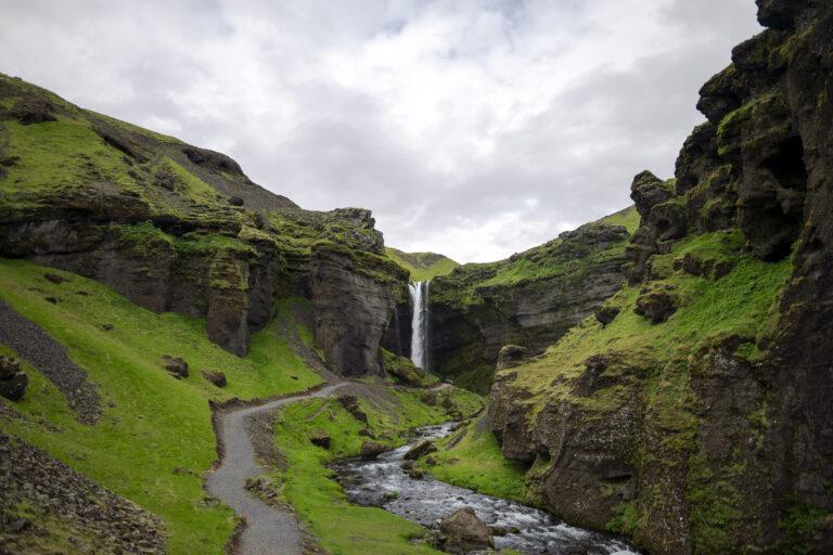 a moss covered gorge that show kvernufoss, one of the best southern iceland waterfalls, in the distance