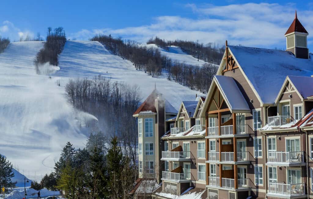 Snow-covered ski slopes at Blue Mountain Resort in Ontario, with chalet-style buildings in the foreground and snowmaking machines operating on the hillside.