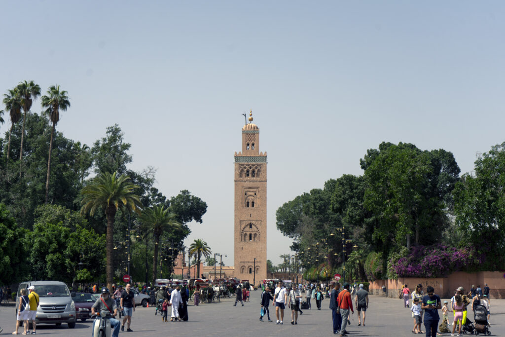 koutoubia mosque in marrakech in the distance surrounded by trees and pedestrians