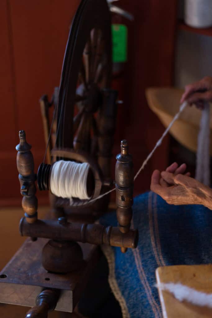 two hands feeding wool into a wooden spinning wheel