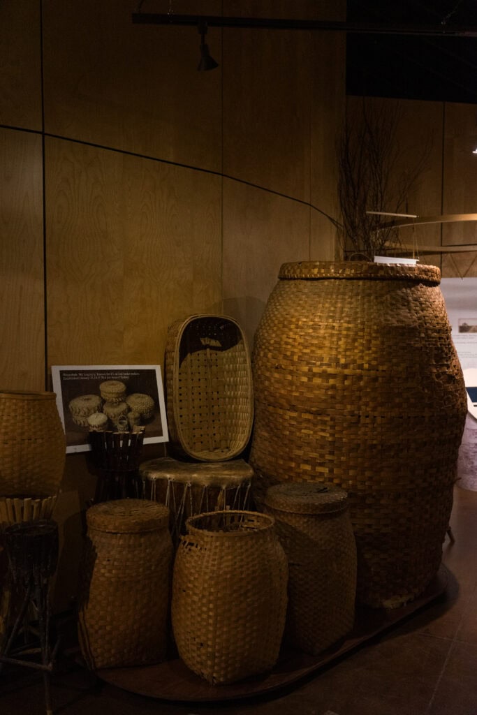 a collection of woven baskets of various sizes up against a wall in a room in a museum