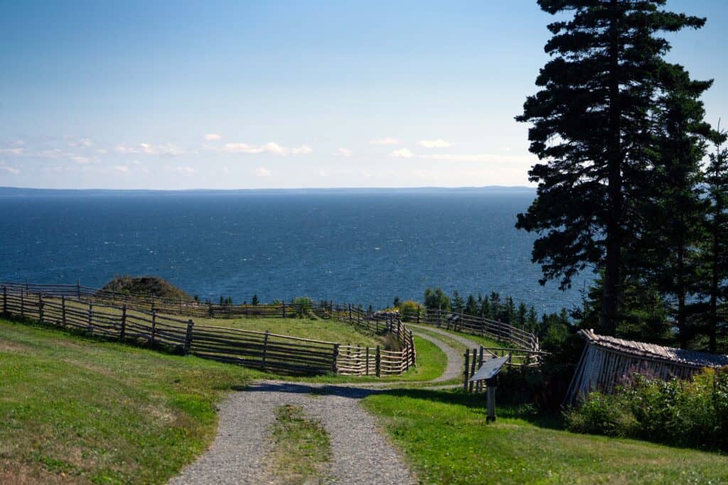 a road with fences on either side leading down a grassy hill toward a big blue lake