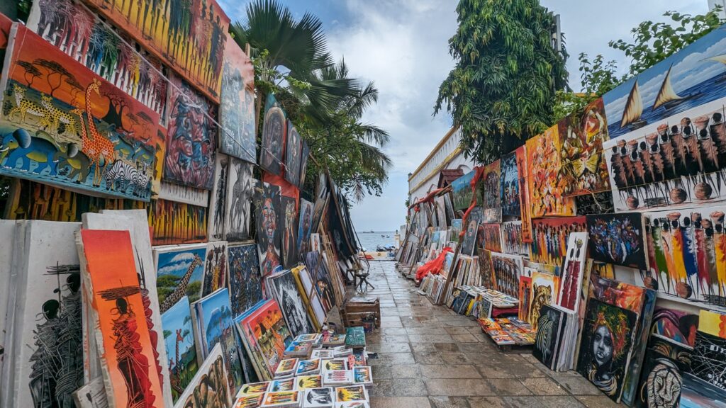 a street leading to the ocean that is lined with tanzanian art, in Stone Town, Zanzibar