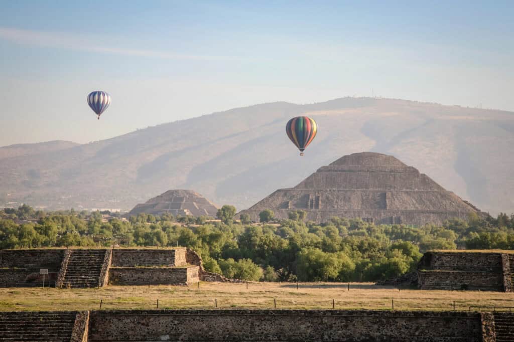 Two colourful hot air balloons floating low overhead of two ancient pyramids at Teotihuacan.