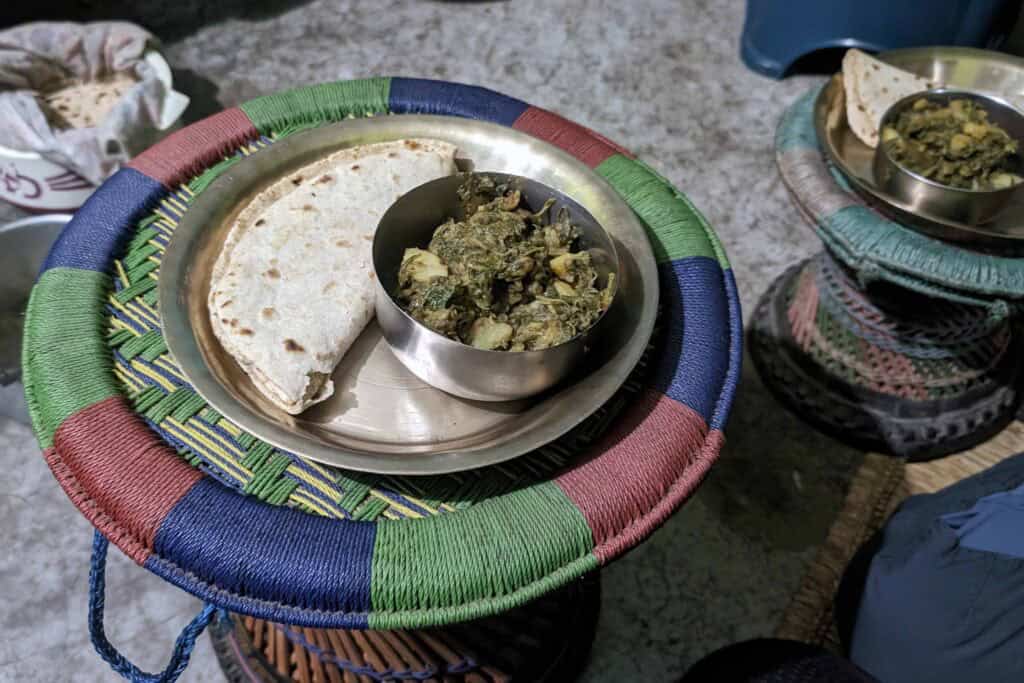 Homemade flatbread served with a bowl of vegetable curry on a metal plate, resting on a colourful woven stool at a homestay in Nepal.