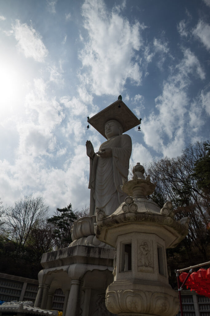 a tall statue of a buddha with a raised hand and clouds behind