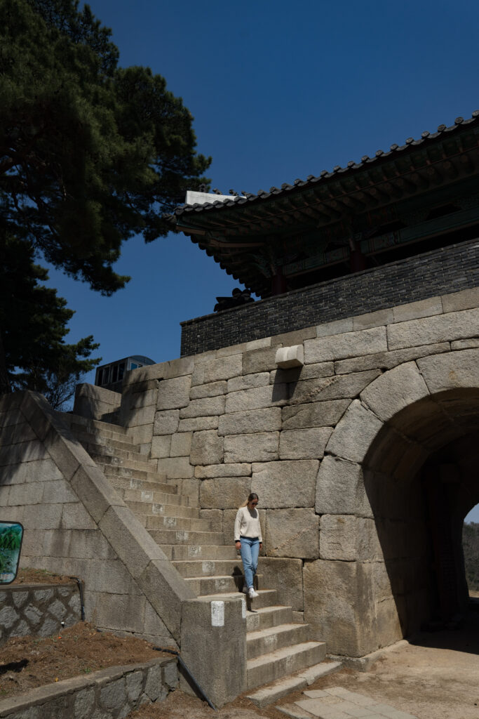 a woman walking down the stone staircase of a historic gate in Seoul, Korea