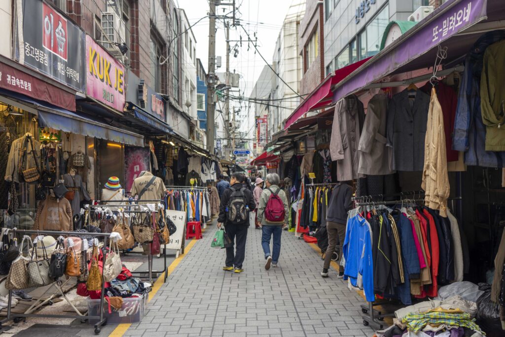 two people walking down a street in Busan with clothing hanging off racks on either side of them