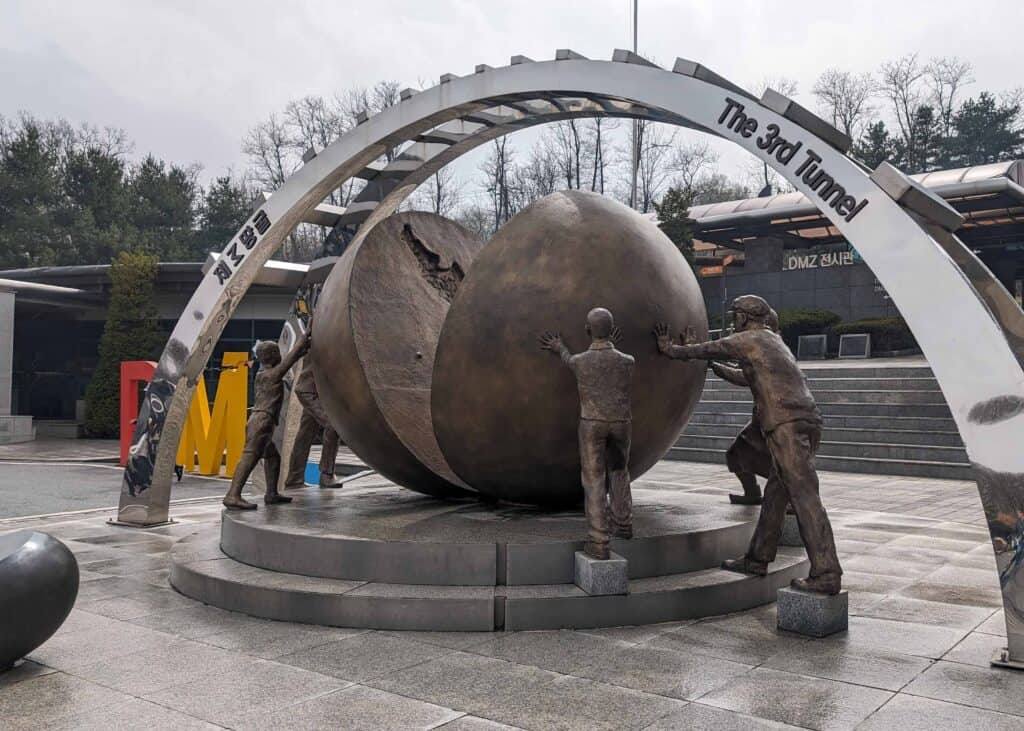 Monument at the Third Infiltration Tunnel in the Korean DMZ, showing bronze figures pushing apart a large stone sphere beneath an arch labeled “The 3rd Tunnel.”