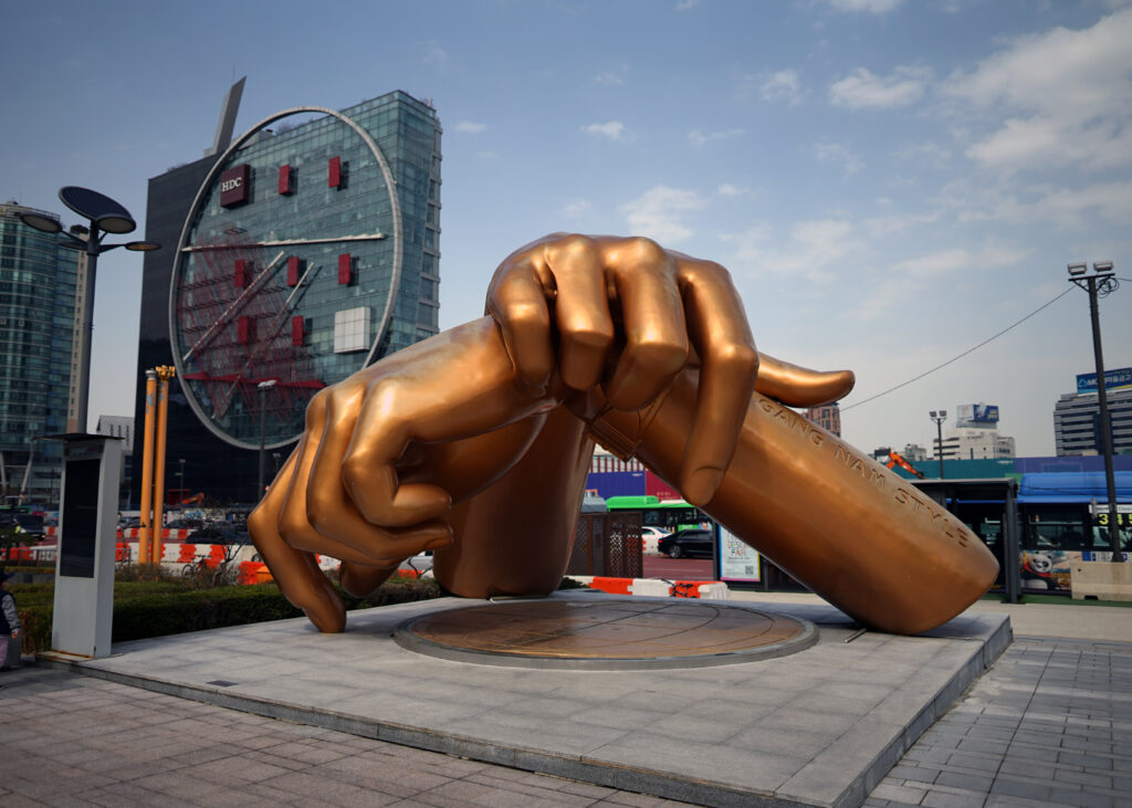 a copper coloured statue of two giant hands crossed over eachother in Gangnam, Seoul, South Korea