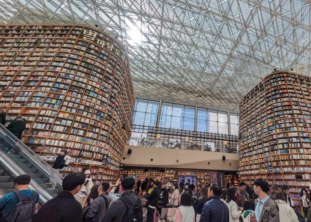 Interior of Starfield Library in COEX Mall, with towering floor-to-ceiling bookshelves, a glass ceiling, and visitors browsing and walking through the open space.