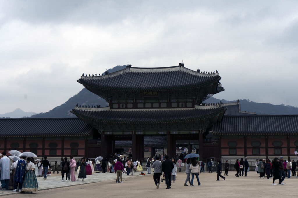 the main palace at Gyeongbokgung Palace, with mountains in the distance and tourists milling around in front of it