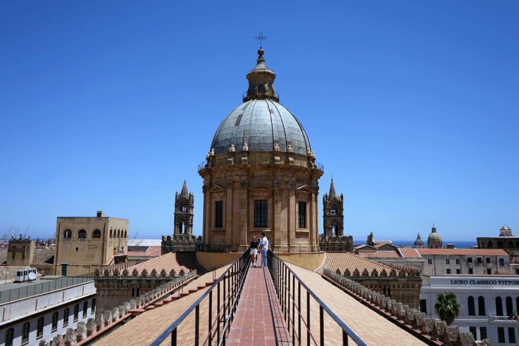 View from the rooftop walkway of Palermo Cathedral looking toward the large central dome under a clear blue sky.