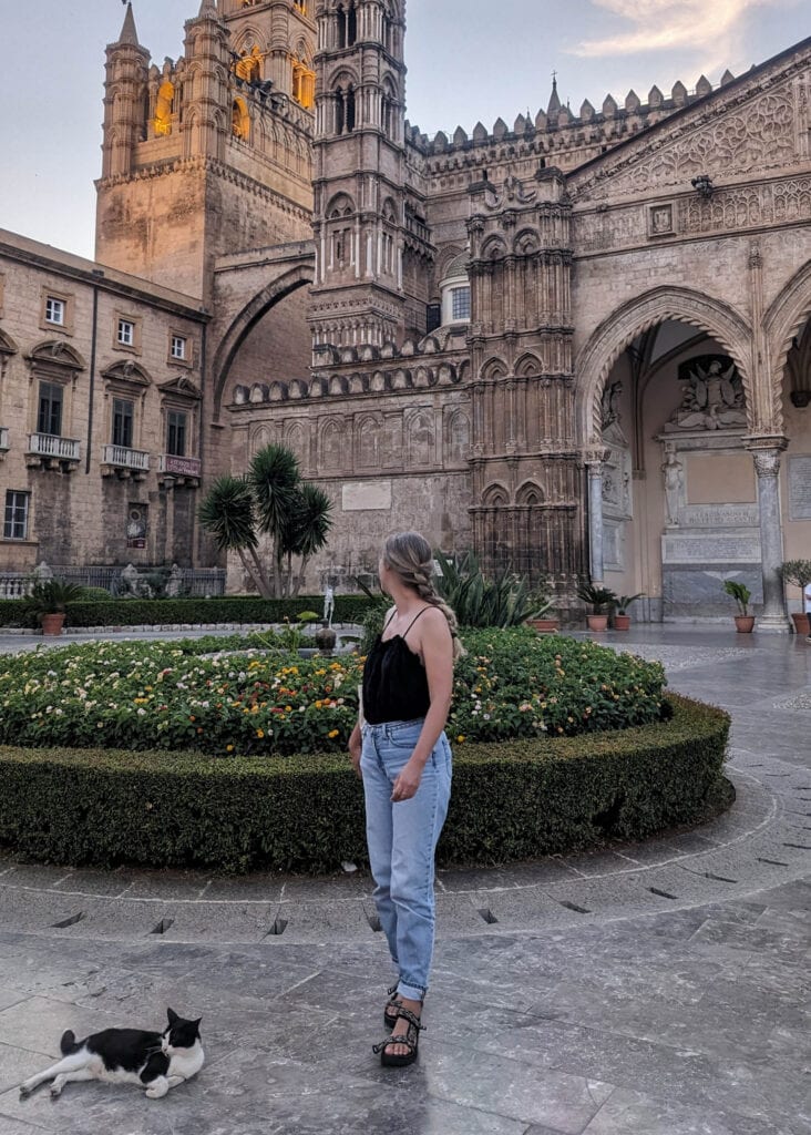 Woman standing in front of Palermo Cathedral in Sicily on a summer evening, with a black and white cat lying next to her