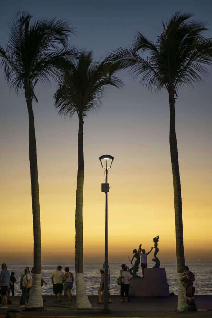 palm trees, and lamp post, and sculptures along the waterfront of puerto vallarta at sunset time