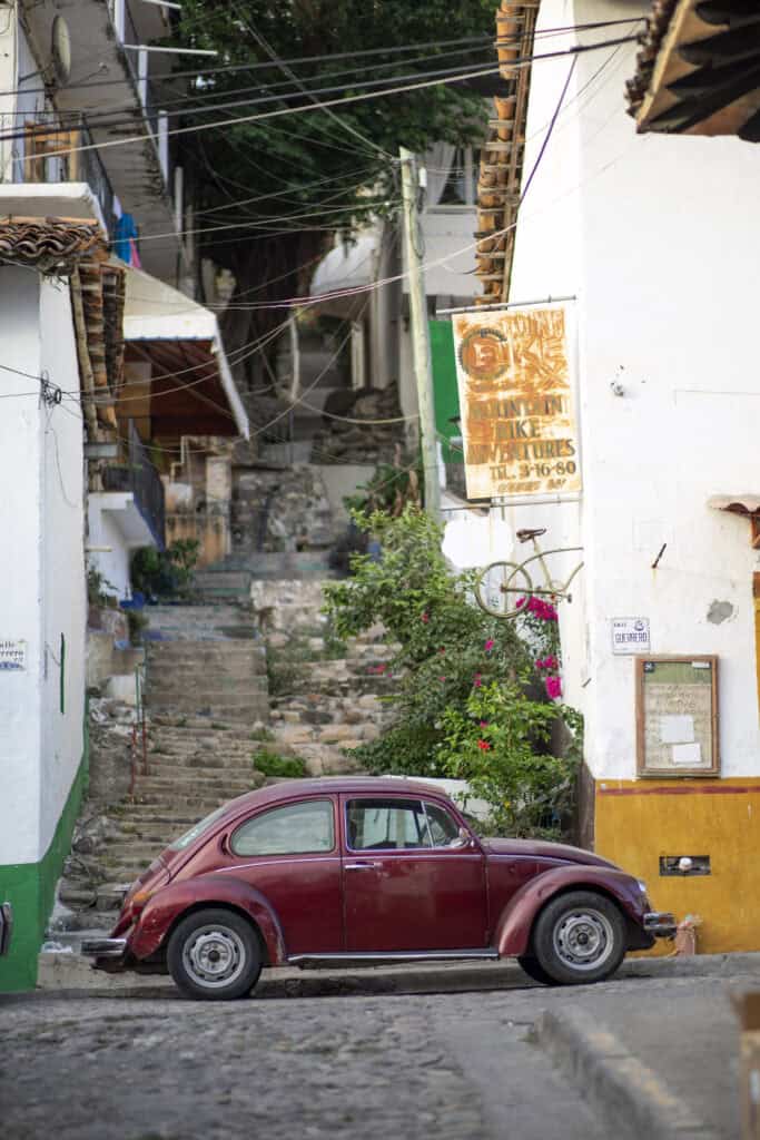 a red vintage beatle car parked on a cobblestone street with a cobblestone staircase behind it