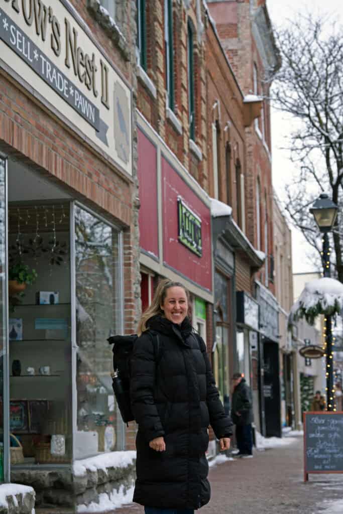 a blonde woman standing on a street in orillia wearing a black jacket, and smiling