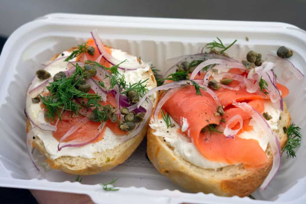 a bagel cut in half and covered in cream cheese, smoked salmon, capers, and greens
