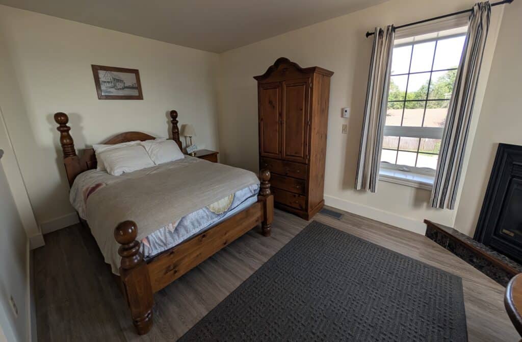 Guest room at the Seacliffe Inn in Leamington, Ontario, featuring a wooden bed, matching wardrobe, large window with natural light, and simple, cozy furnishings in a historic waterfront inn.