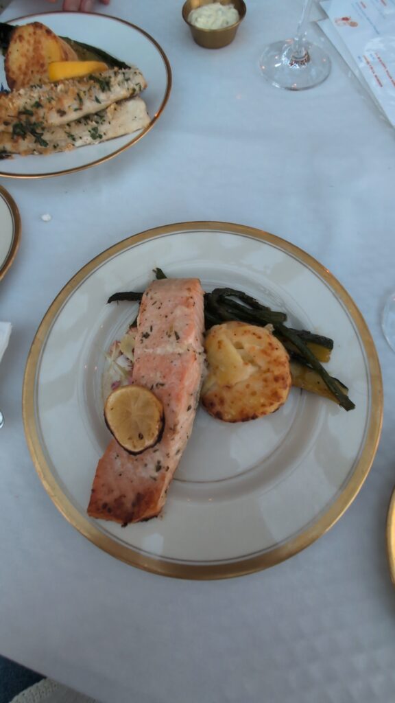 a plate of oysters, a cocktail, and a plate of salad a salmon on a white table cloth