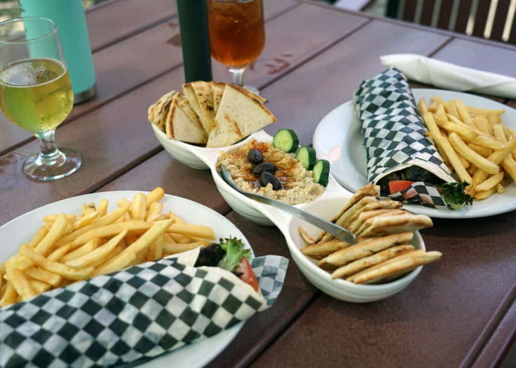 Outdoor patio table at Freddy's Restaurant in Leamington featuring kafta wraps served with fries, hummus topped with olives, pita bread, fresh vegetables, and drinks, showcasing the restaurant's Lebanese-inspired cuisine.