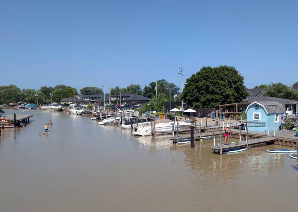 people paddleboarding on SUPs on a calm creek, with lots of boats moored along the shore