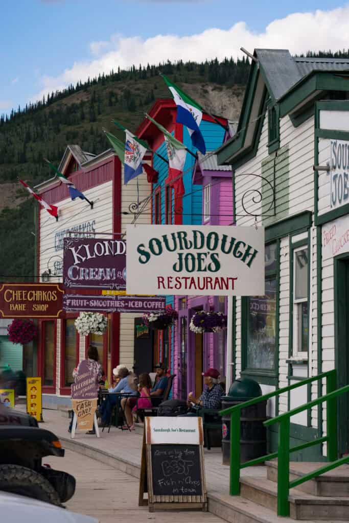 a sidewalk lined with colourful buildings and street signs in Dawson City, Yukon