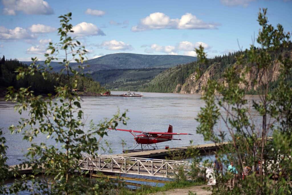 a small red seaplane parked on a dock along the yukon river in dawson city