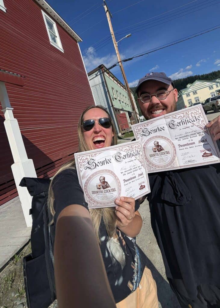 a man and a woman smiling and holding certificates for the Sourtoe Cocktail Club