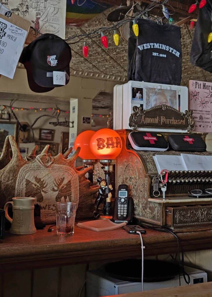 a red lamp that reads "BAR" sitting on top of a counter next to an antique cash register and merch for "Westminster"