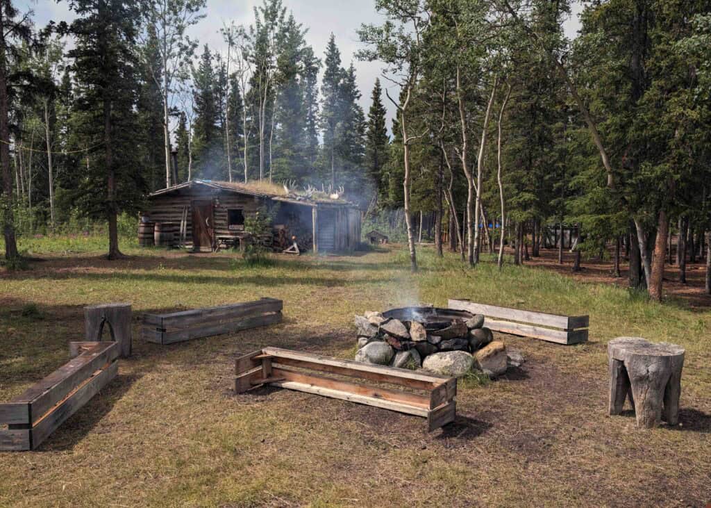 a fire pit with seating around it, and a small log cabin behind it, surrounded by trees, at Long Ago People's Place