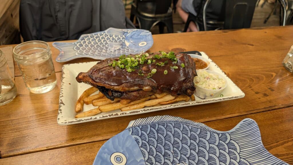 a plate on a wooden table with a large rack of ribs on it, piled on top of fries