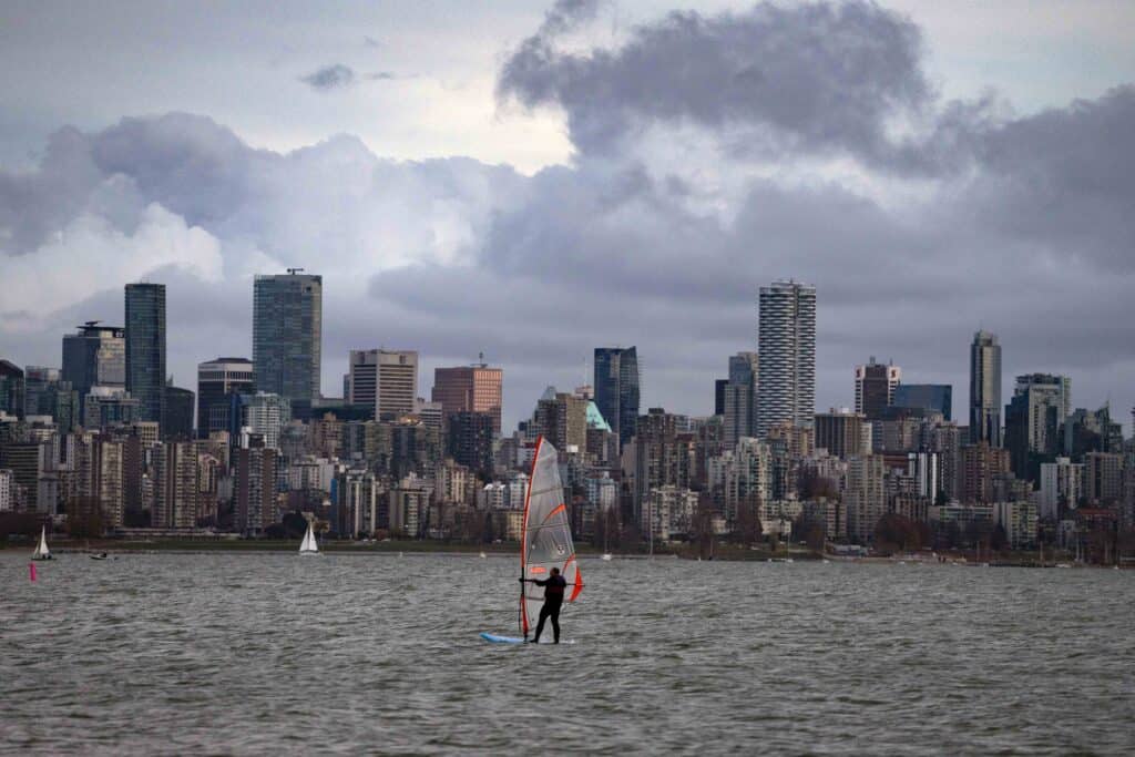 Windsurfer on the water with Vancouver skyline and cloudy mountains in the background.