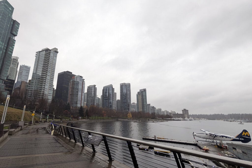 Vancouver Seawall along Coal Harbour with downtown skyline, marina, and cloudy winter sky.