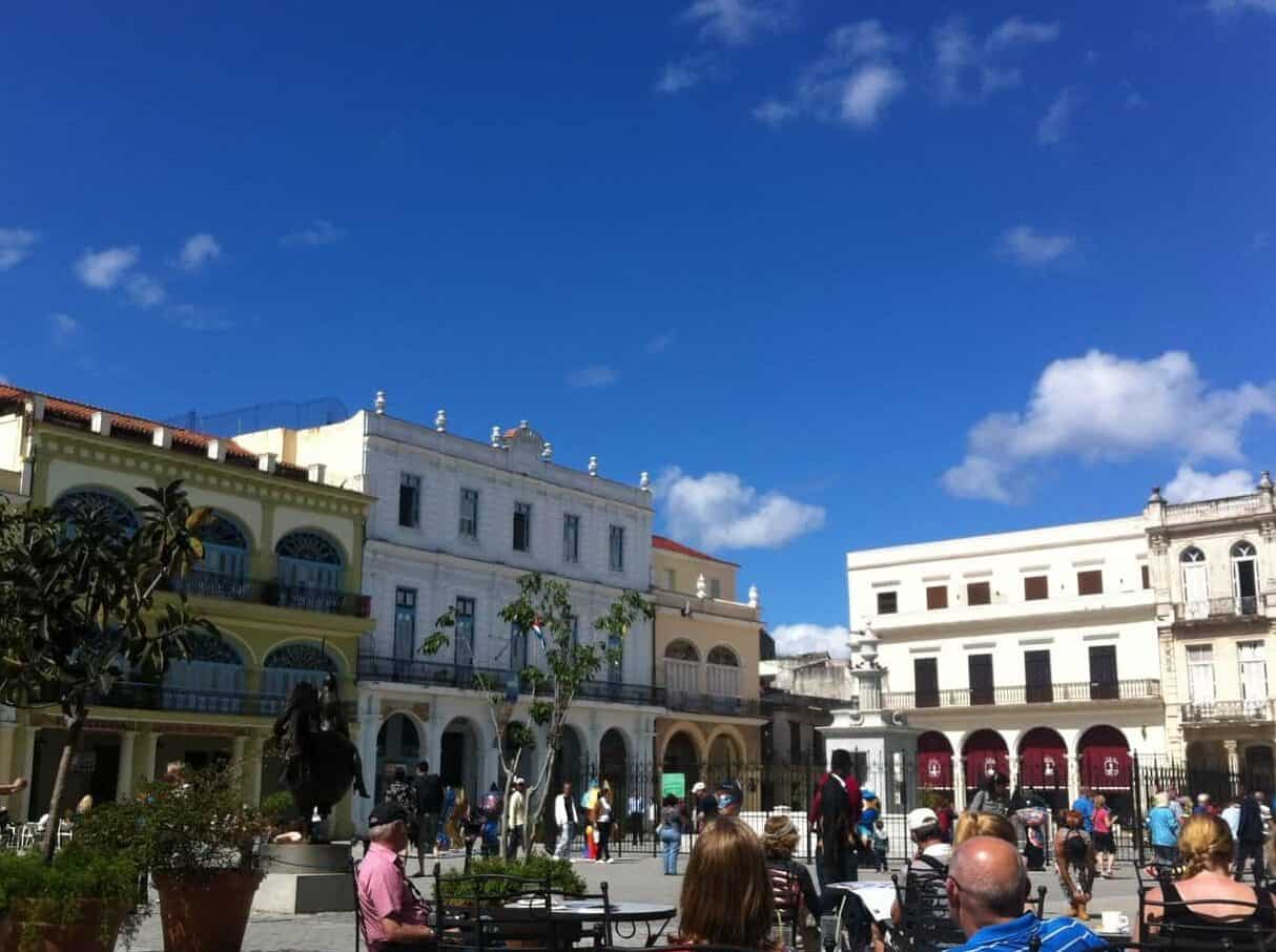 A square in Havana, Cuba, surrounded by historic buildings and with tourists enjoying coffee at tables.