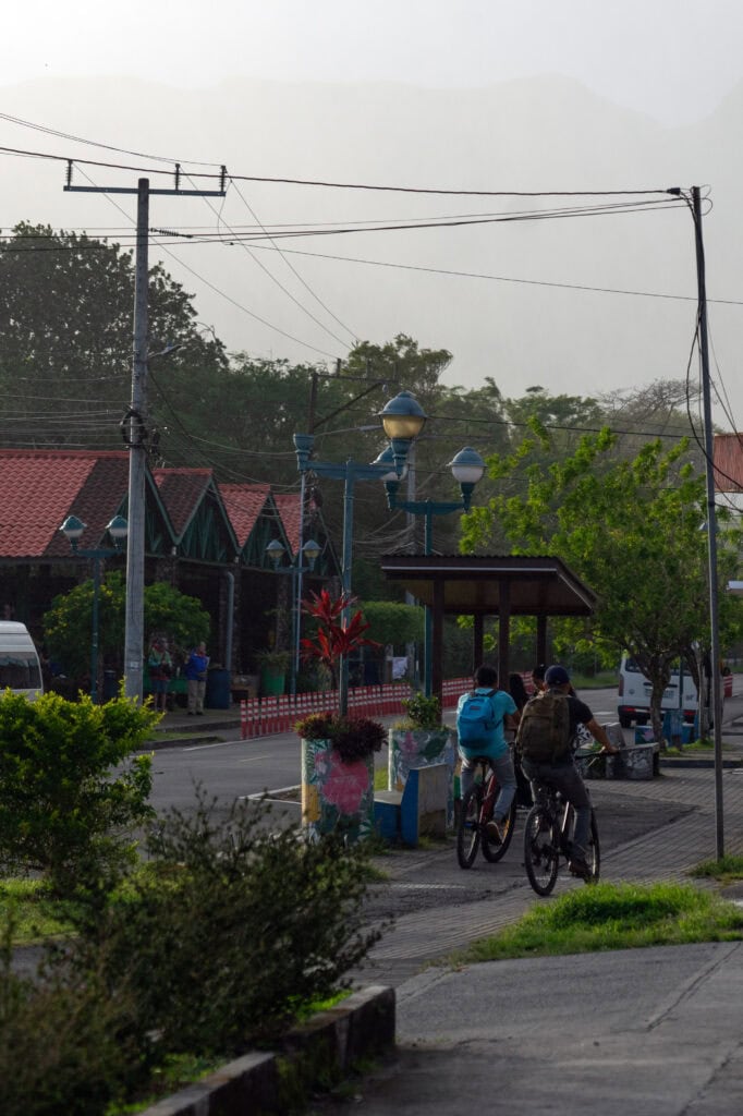 Cyclists riding through the streets of El Valle de Anton, Panama, with misty mountains visible in the background.