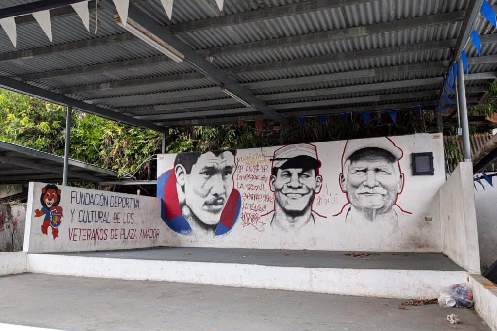 A painted mural on a concrete wall in Panama City’s El Chorrillo neighborhood shows three black-and-white portraits of men wearing caps, alongside the text “Fundación Deportiva y Cultural de los Veteranos de Plaza Amador,” under a covered outdoor structure.