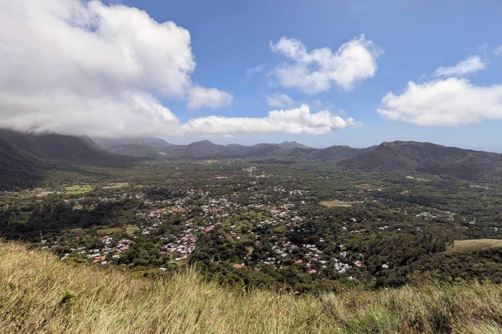 Panoramic view of El Valle de Antón nestled inside a volcanic crater, surrounded by lush green hills and mountains under a partly cloudy blue sky.