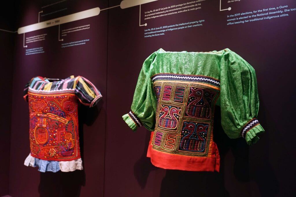 Traditional Guna dresses displayed on a museum wall in Panama, featuring brightly colored molas with intricate stitched patterns and geometric designs.