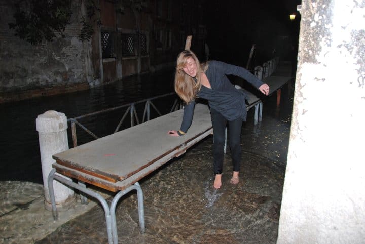 Woman standing barefoot in floodwater during acqua alta in Venice, Italy at night.