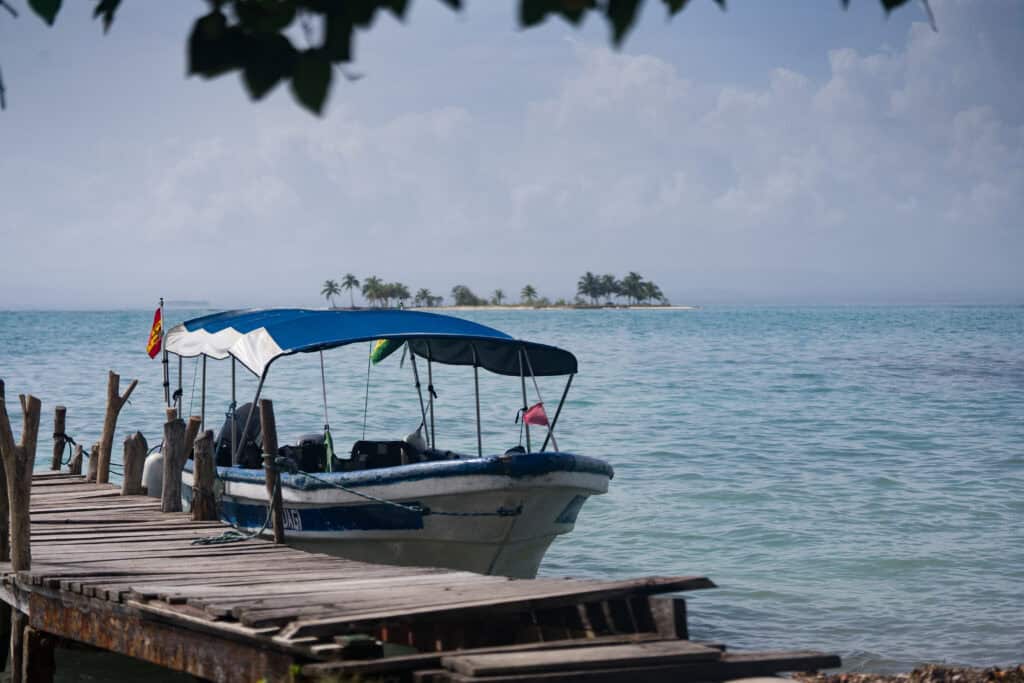 Small motorboat docked at a wooden pier in Guna Yala, Panama, with calm Caribbean water and a palm-covered island in the distance.